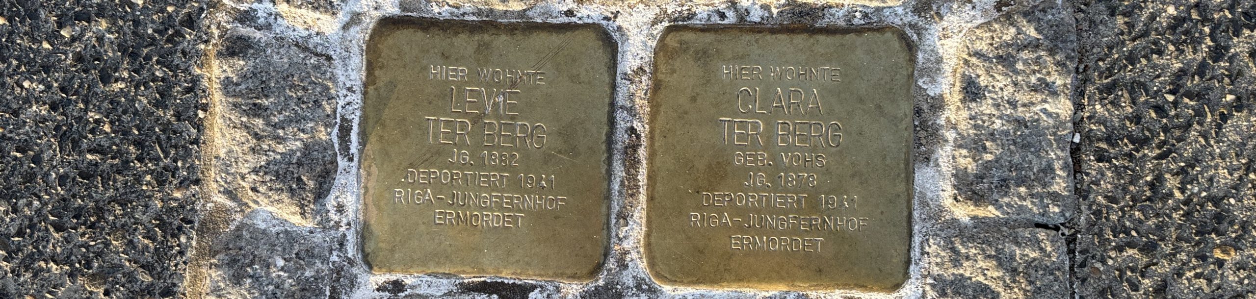 Blick auf zwei in den Boden eingebaute Stolpersteine. Sie tragen die Inschriften Hier wohnte Levie ter Berg Jg. 1892 Deportiert 1941 Riga-Jungfernhof Ermordet Hier wohnte Clara ter Berg Geb. Vohs Jg. 1878 Deportiert 1941 Riga-Jungfernhof Ermordet